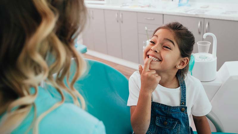 little girl pointing to dental crown in mouth dental sealants in Wheaton and St. Charles