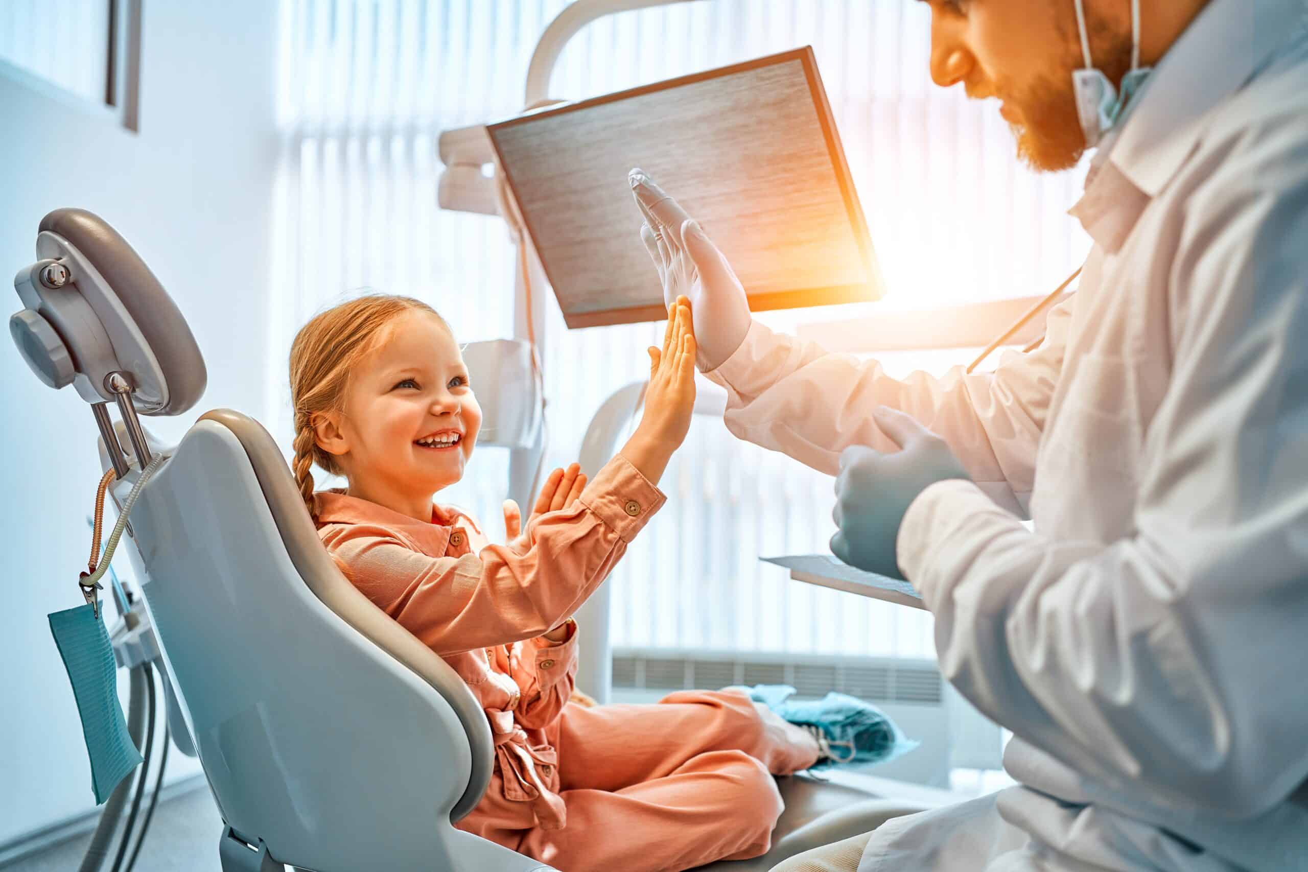 Little girl sitting in a dentist's chair smiling and giving a thumbs-up – Pediatric Dentist Near Me